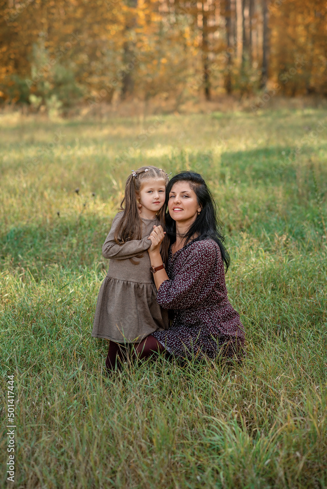 Fototapeta premium mother and daughter are hugging and smiling, sitting on the grass in the park