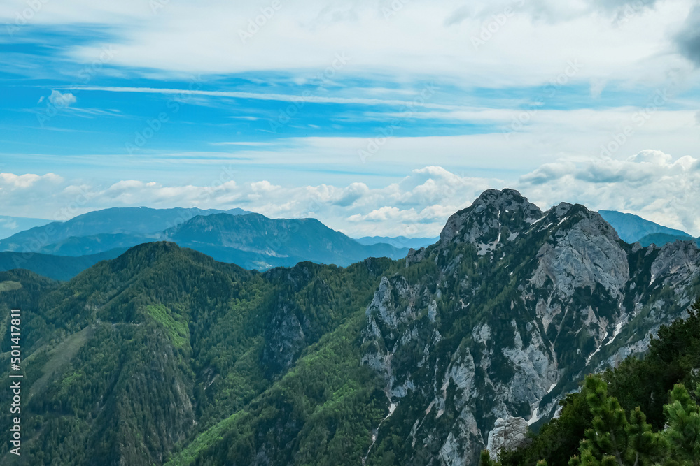 Obraz premium Panoramic view from the summit of Goli Vrh on rocky sharp mountains of Kamnik Savinja Alps in Carinthia, border Austria and Slovenia. Green spring meadow in Vellacher Kotschna. Mountaineering. Freedom
