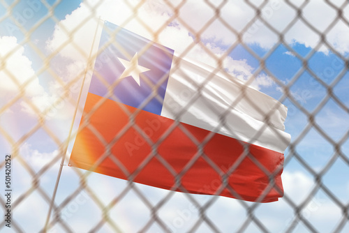 A steel mesh against the background of a blue sky and a flagpole with the flag of chile