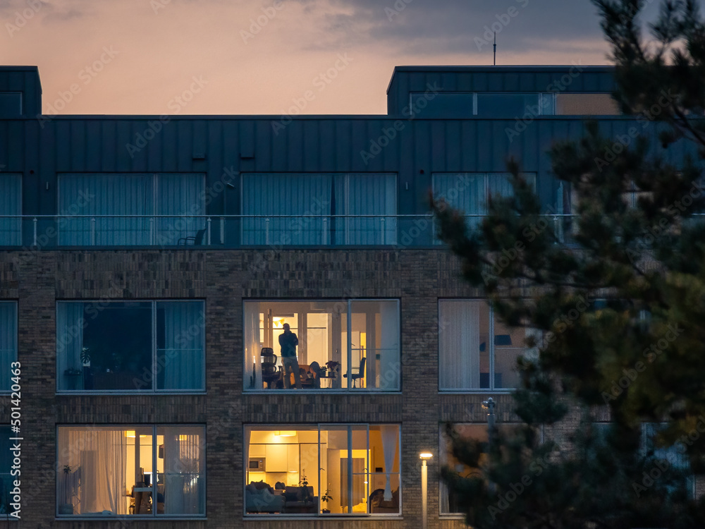 Man Looking Out the Window of an Apartment at Sunset, Ireland Man Looking Out the Window of an Apartment at Sunset, Ireland