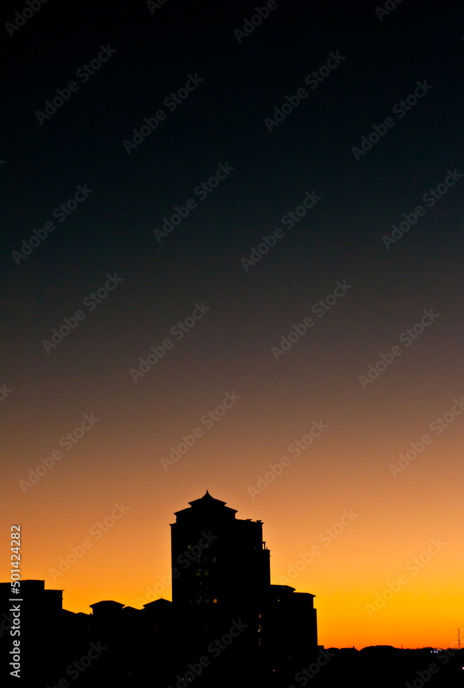 front view, far distance of a building in silhouette at sunset with a cloudless sky