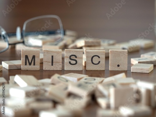 the acronym misc. for miscellaneous word or concept represented by wooden letter tiles on a wooden table with glasses and a book photo