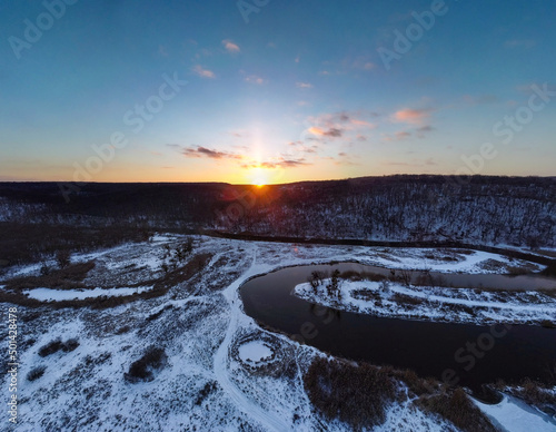 Winter aerial wide panorama view on snowy river curve with scenic reflection. Zmiyevsky region on Siverskyi Donets River in Ukraine. Sunset sun shining above woody hill