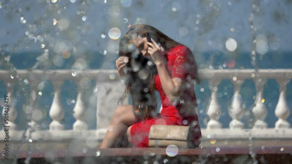 Brunette woman called up with her smartphone behind a fountain Brunette woman called up with her smartphone behind a fountain