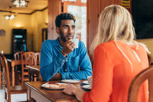 Colombian man listens attentively to a white woman while drinking coffee