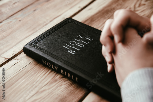 man praying with hands crossed and Holy Bible