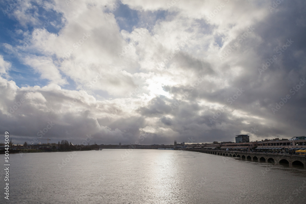 Winter Panorama of the estuary of the garonne river seen from Garonne quay (Quais de la Garonne) in bordeaux, France, with the old buildings of the city center in background and a cloudy gray sky.....