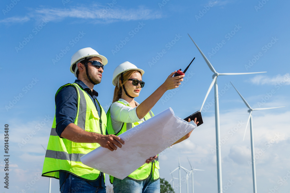 Asian man and woman engineers working on site in wind turbine on the background. Young people engineers working at renewable energy farm Asian man and woman engineers working on site in wind turbine on the background. Young people engineers working at renewable energy farm