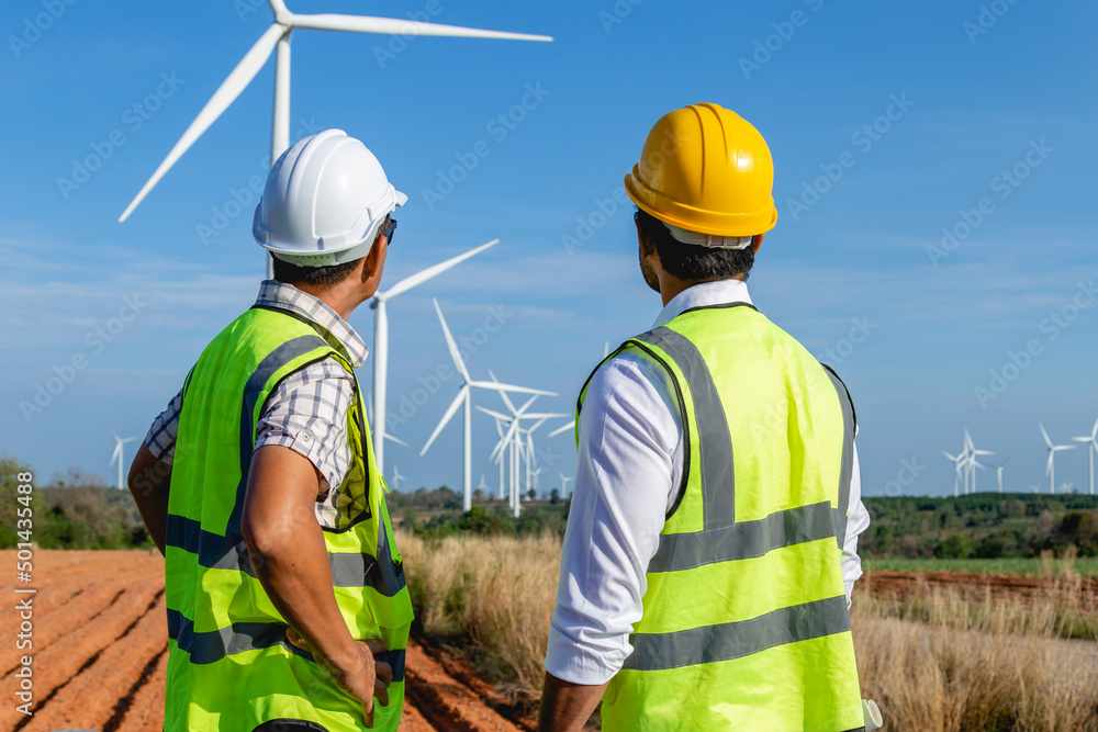 Back view of two Asian engineers discussing against turbines on wind turbine farm. Back view of two Asian engineers discussing against turbines on wind turbine farm.