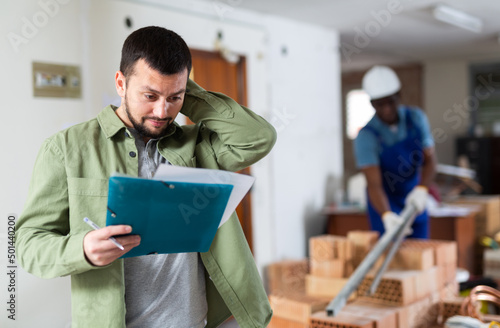 Young engineer working on a construction site indoors holds a folder with documents while studying them