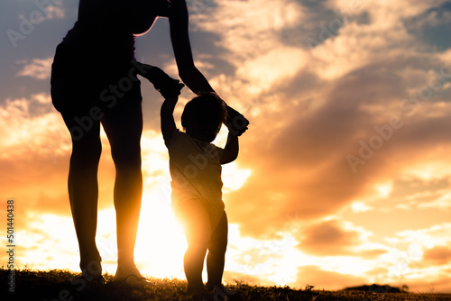 silhouette of other teaching her child to walk, baby steps, parenting concept. 