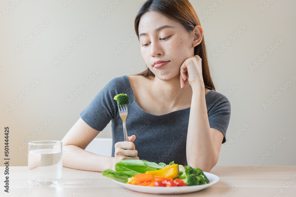 unhappy asian women is on dieting time looking at broccoli on the fork. girl do not want to eat vegetables and dislike taste unhappy asian women is on dieting time looking at broccoli on the fork. girl do not want to eat vegetables and dislike taste