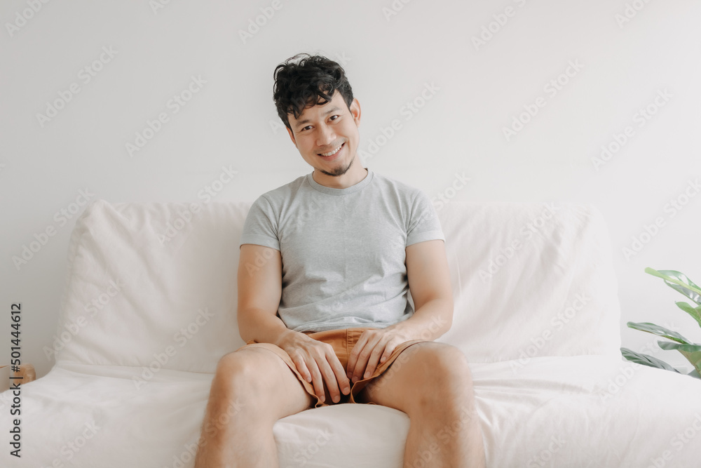 Happy Asian man sits on the sofa in his apartment. Concept of casual and relax.