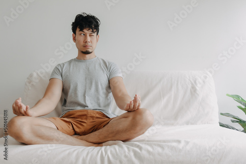 Asian man does meditation on the sofa with little distraction in his apartment. photo