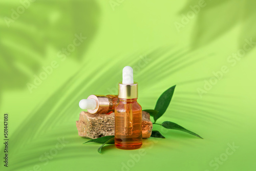 Bottles of natural serum, stone and leaves on green background