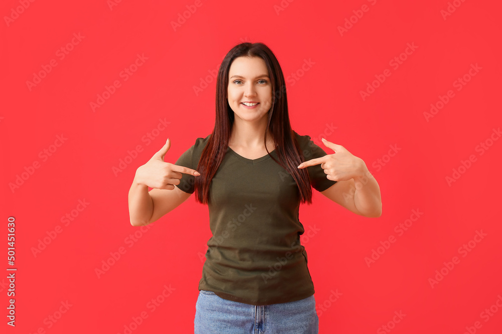 Young woman pointing at t-shirt on red background Young woman pointing at t-shirt on red background