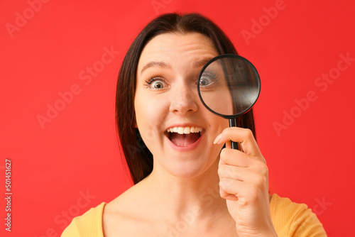 Surprised young woman with magnifier on red background, closeup