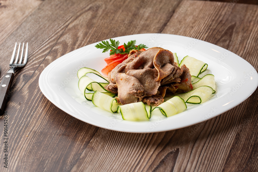 Serving a dish from the restaurant menu. Sliced beef tongue with cucumber on wooden background, a delicious appetizer