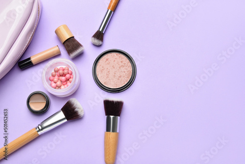 Makeup brushes and cosmetic products on purple background