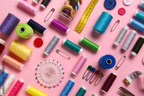 Thread spools, ball pins, measuring tape and buttons on pink background