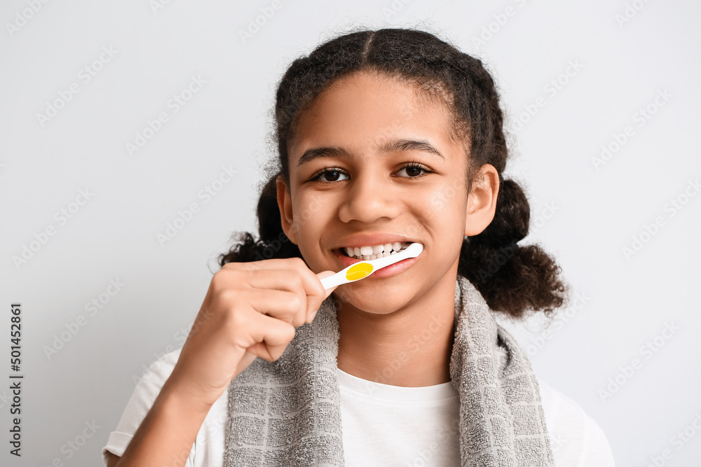 African-American teenage girl brushing teeth on light background African-American teenage girl brushing teeth on light background