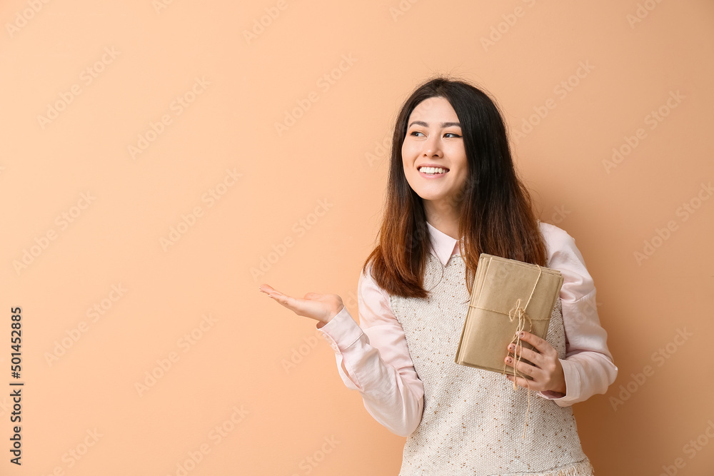 Young Asian woman with stack of invitations showing something on beige background Young Asian woman with stack of invitations showing something on beige background