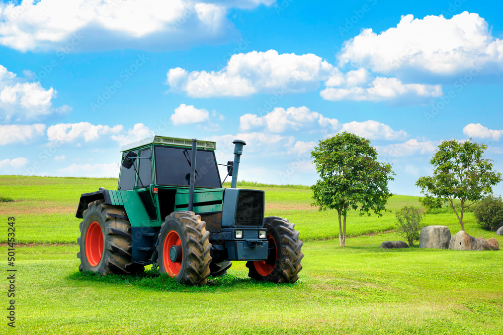 Obraz premium A green tractor is parked on a lawn and behind it is a beautiful cloudy sky. Concept. Antique tractor with beautiful garden decorations.