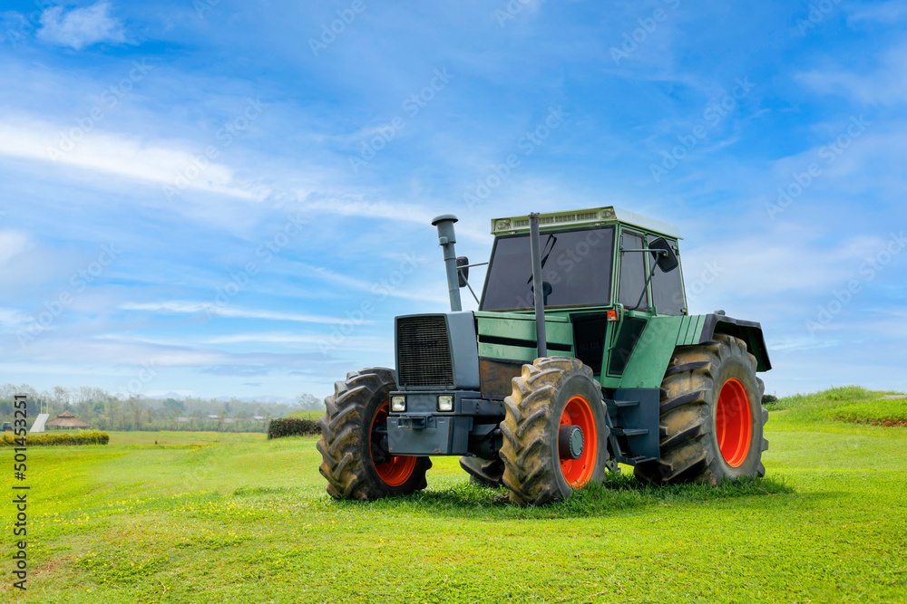 A green tractor is parked on a lawn and behind it is a beautiful cloudy sky. Concept. Antique tractor with beautiful garden decorations. A green tractor is parked on a lawn and behind it is a beautiful cloudy sky. Concept. Antique tractor with beautiful garden decorations.