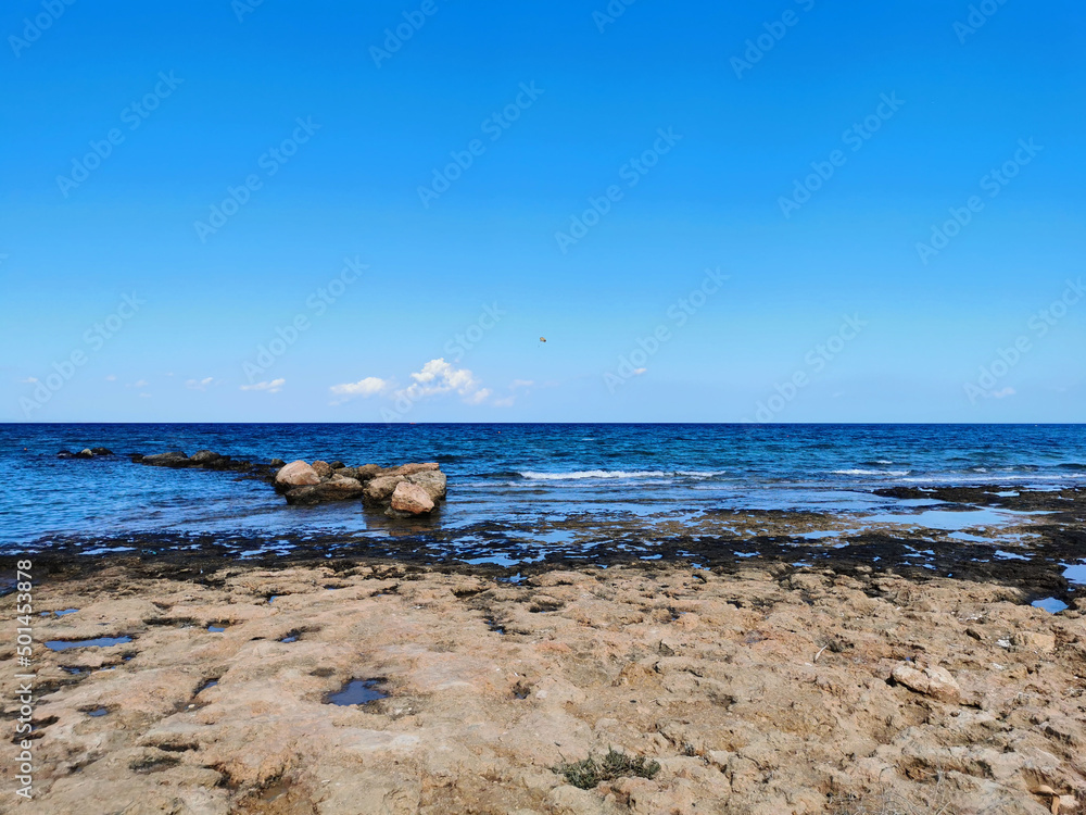 Fototapeta premium The coast of the Mediterranean Sea, waves, clear water, a stone ridge against a blue sky with clouds.