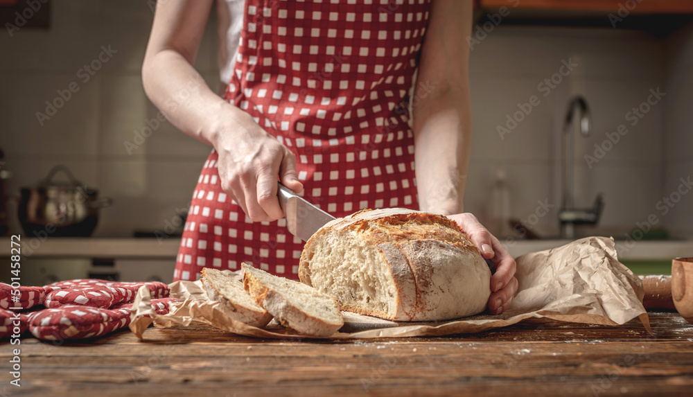 Hands cut with a knife homemade natural fresh bread with a Golden crust on wooden background. Baking bakery products