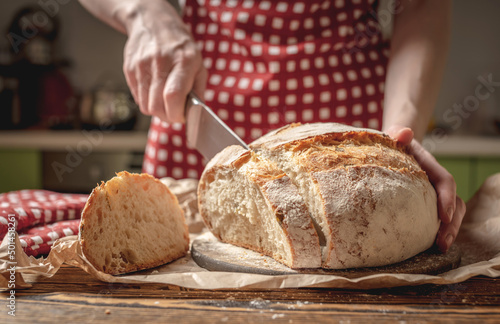 Hands cut with a knife homemade natural fresh bread with a Golden crust on wooden background. Baking bakery products