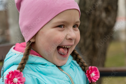 Portrait of a mischievously happy girl with her tongue out. Five-year-old child with long hair braided into pigtails.