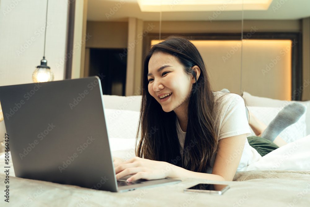 Asian woman laying on her laptop while enjoying herself in bed in her bedroom at home. Asian woman laying on her laptop while enjoying herself in bed in her bedroom at home.