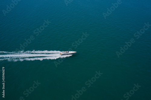 Drone view of a boat sailing at high speed. Aerial view of a boat in motion on blue water. Top view of a white boat sailing in the blue sea. © Berg