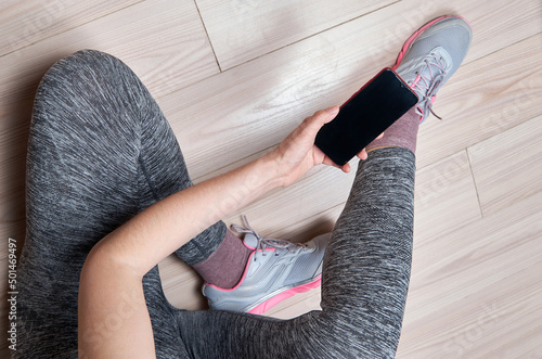 Woman in sportswear and sport shoes with mobile phone sitting on floor