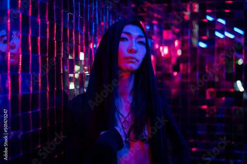 Close-up portrait of an androgenic model in a hood. Male transgender in studio with neon light.
