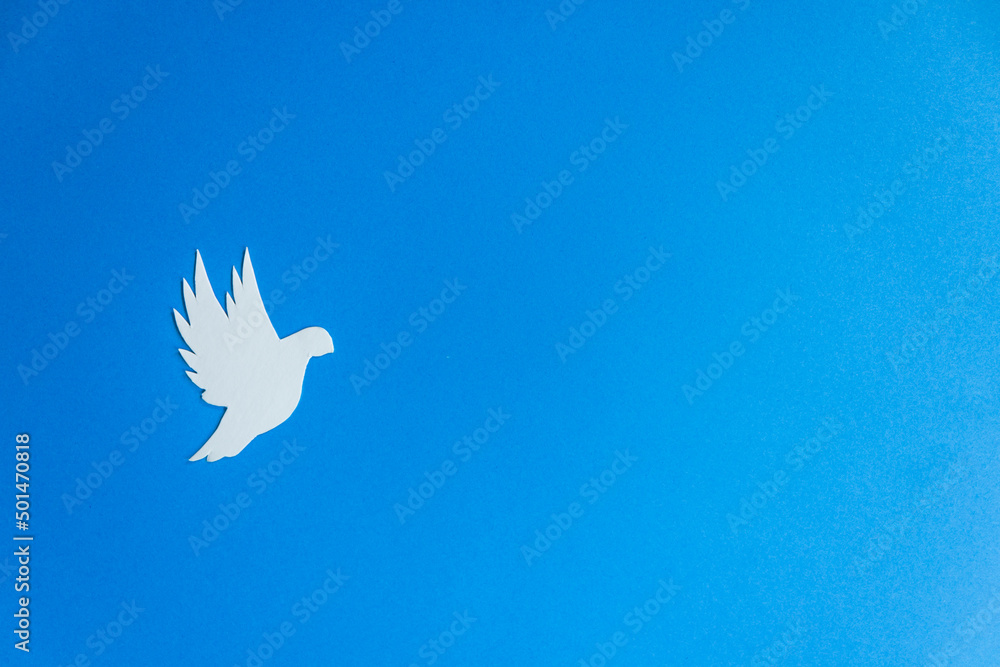 White paper dove bird as a symbol of peace isolated on blue background. Peace to Ukraine. International Day of Peace. White paper dove bird as a symbol of peace isolated on blue background. Peace to Ukraine. International Day of Peace.