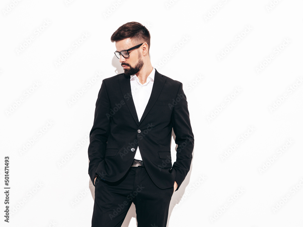 Portrait of handsome confident stylish hipster lambersexual model. Sexy modern man dressed in elegant black suit. Fashion male posing in studio near white wall. Isolated Portrait of handsome confident stylish hipster lambersexual model. Sexy modern man dressed in elegant black suit. Fashion male posing in studio near white wall. Isolated
