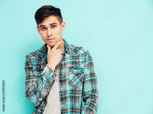 Portrait of handsome smiling model. Sexy stylish man dressed in checkered shirt and jeans. Fashion hipster male posing near blue in studio. Isolated