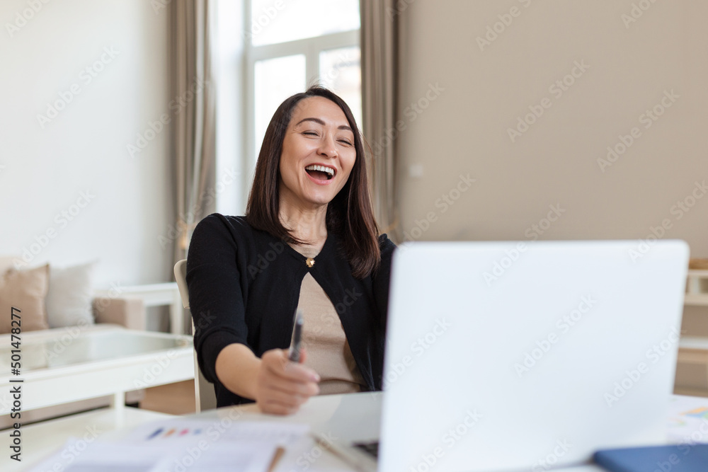 Asian woman working on laptop computer, smiling. Woman Working From Home On Laptop In Modern Apartment. Trendy woman working on laptop from home Asian woman working on laptop computer, smiling. Woman Working From Home On Laptop In Modern Apartment. Trendy woman working on laptop from home