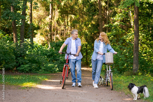Active old age, people and lifestyle concept happy senior couple fixing bike, talking on summer city park on path in sunny forest, wearing casual clothes cute caucasian man and woman #501478695