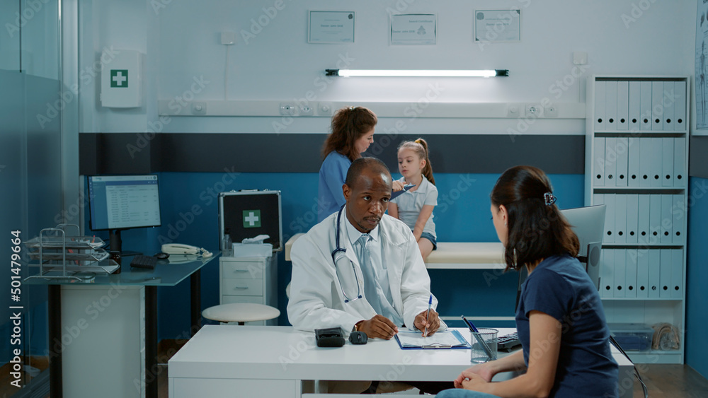 Obraz premium Physician having conversation with adult in medical cabinet, taking notes about health care diagnosis. General practitioner talking to mother about recovery treatment at appointment.