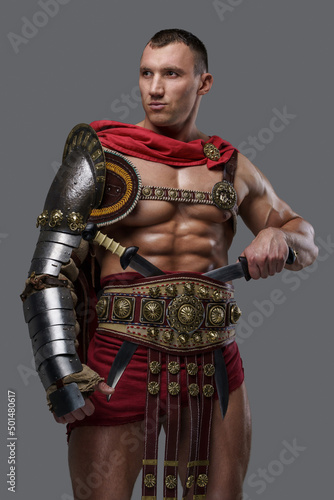 Portrait of naked gladiator champion with dual swords dressed in light armor isolated on grey.