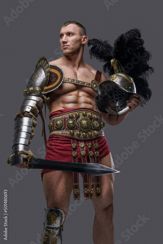 Shot of legendary roman warrior with muscular build holding gladius and plumed helmet.