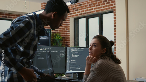 Cuadro en lienzo Junior developer sitting down on desk showing laptop with source code to senior dev asking for opinion