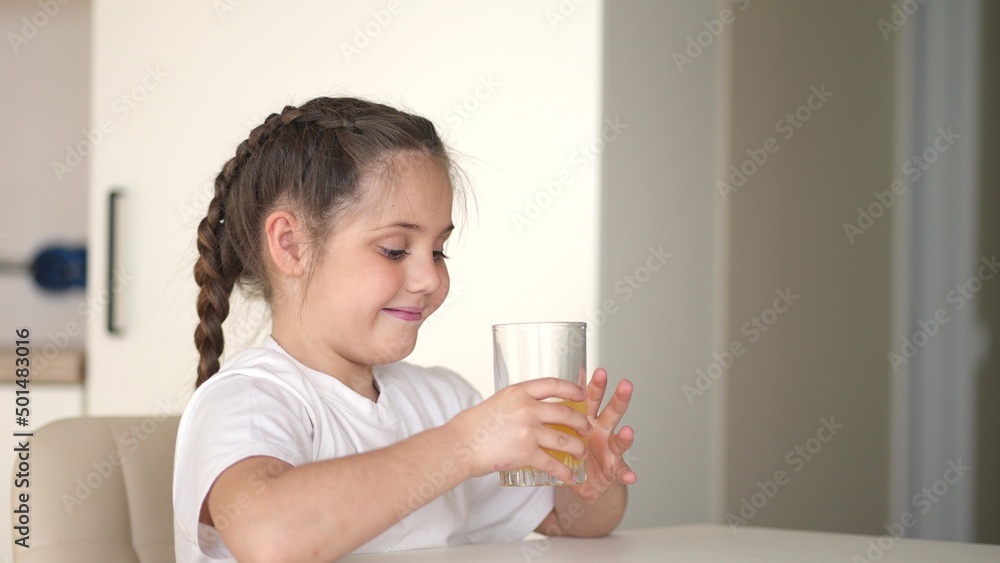 girl child drinking juice. happy family a healthy eating kid dream indoors concept. daughter girl drinking yellow juice from a glass cup in the kitchen. child drinking fruit juice girl child drinking juice. happy family a healthy eating kid dream indoors concept. daughter girl drinking yellow juice from a glass cup in the kitchen. child drinking fruit juice