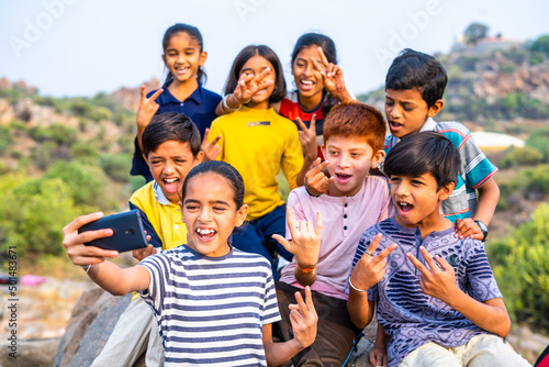Group of kids in cheerful taking selfie on mobile phone at hill top after reaching destination on hill top - concept of friendship, holidays, outdoor activities and summer camp. © WESTOCK