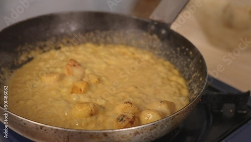 Delicious creamy coconut curry seafood scallops simmering on shallow frying pan with aromatic smell, close up shot professional chef cooking concept.