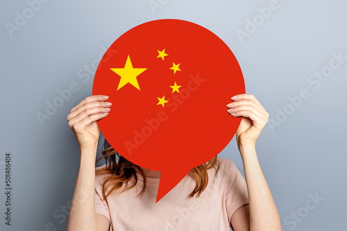Female student holds blank white speech bubble with Chinese flag isolated over grey studio background. woman holding a round information piece of paper dialog