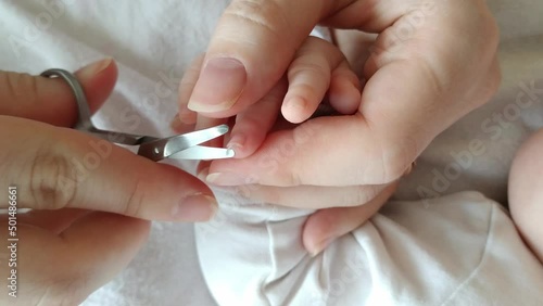 Cutting baby infant newborn nails in bed, father mother hands using scissors to trim son's finger nails, top view handheld, interior, day photo